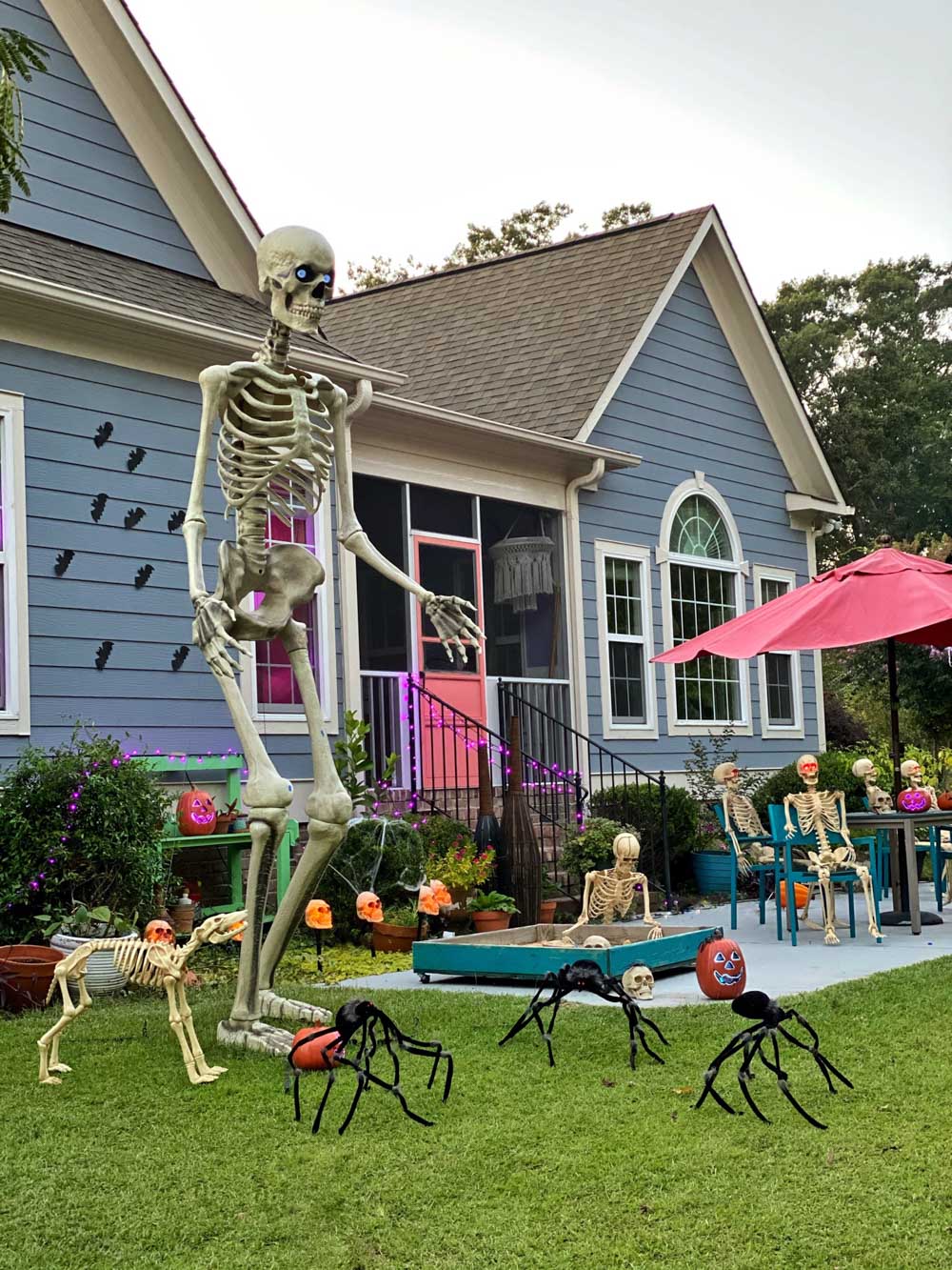 A front yard decorated for Halloween with skeletons, spiders, purple lights, and a giant skeleton.