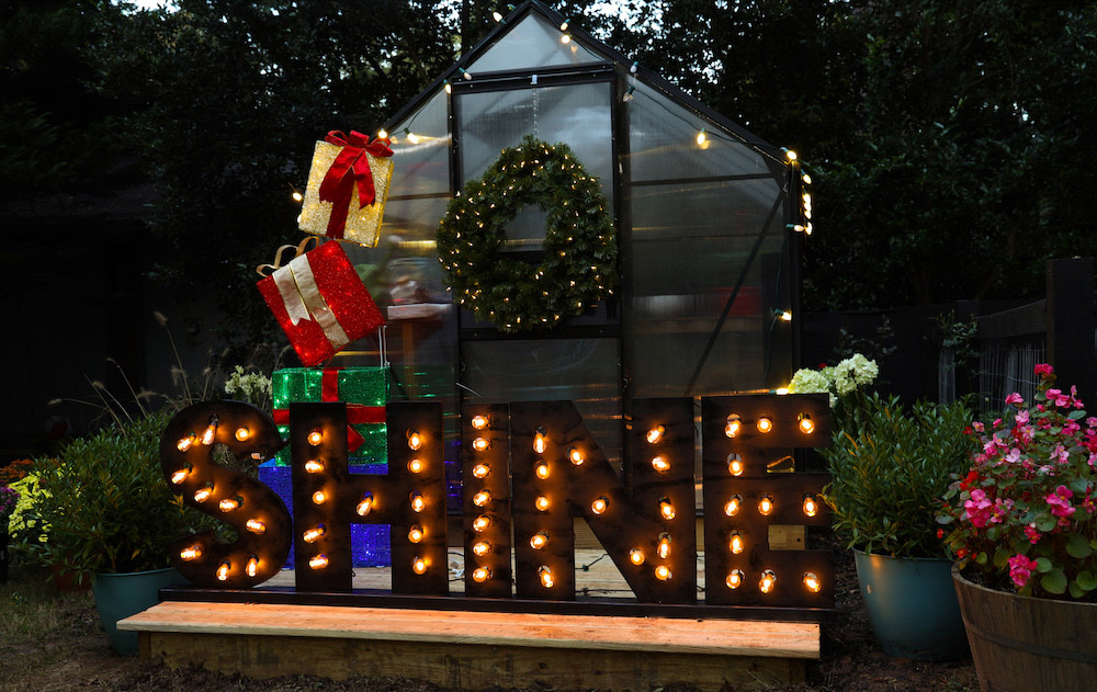 Greenhouse styled with lights, gift box set, marquee sign and pre-lit wreath shot from right