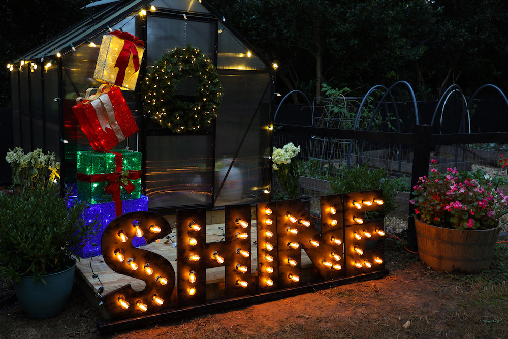 Greenhouse and garden styled with lights, gift box set, marquee sign and pre-lit wreath shot from left