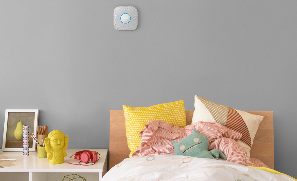 A smoke detector above a bed in a child's room.