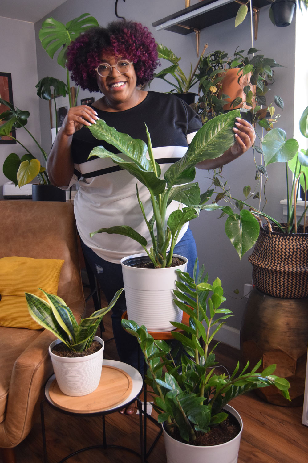  A woman standing behind multiple plants and holding leaves.