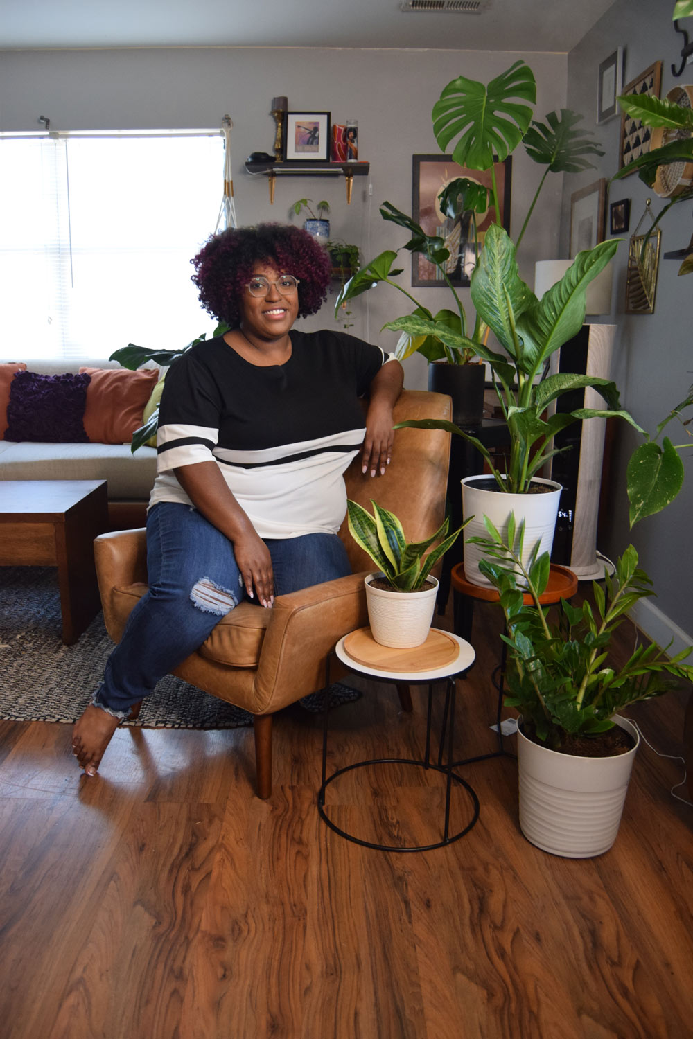A woman sitting in a chair surrounded by plants in a living room.
