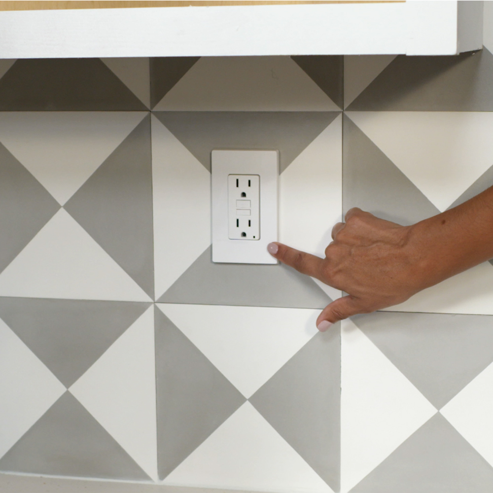 A hand pointing to an outlet on a tiled wall