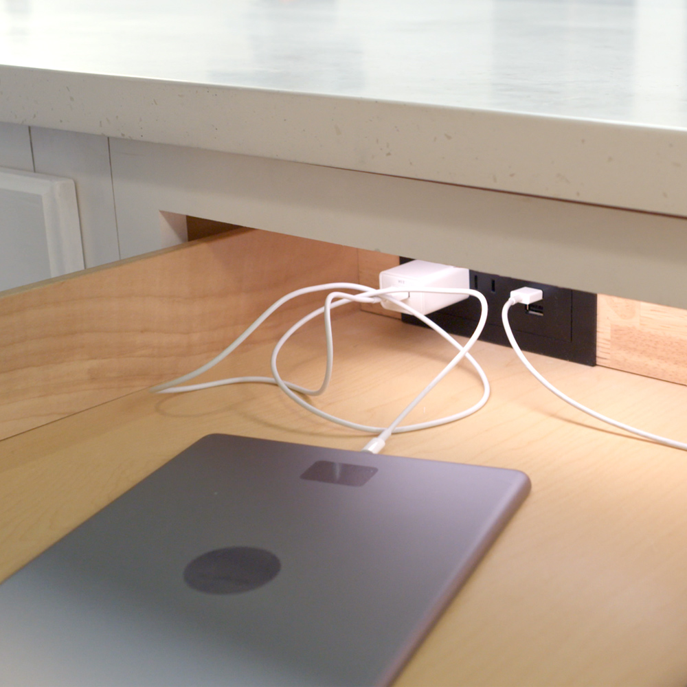 A hidden outlet setup placed in an open counter drawer with devices plugged in