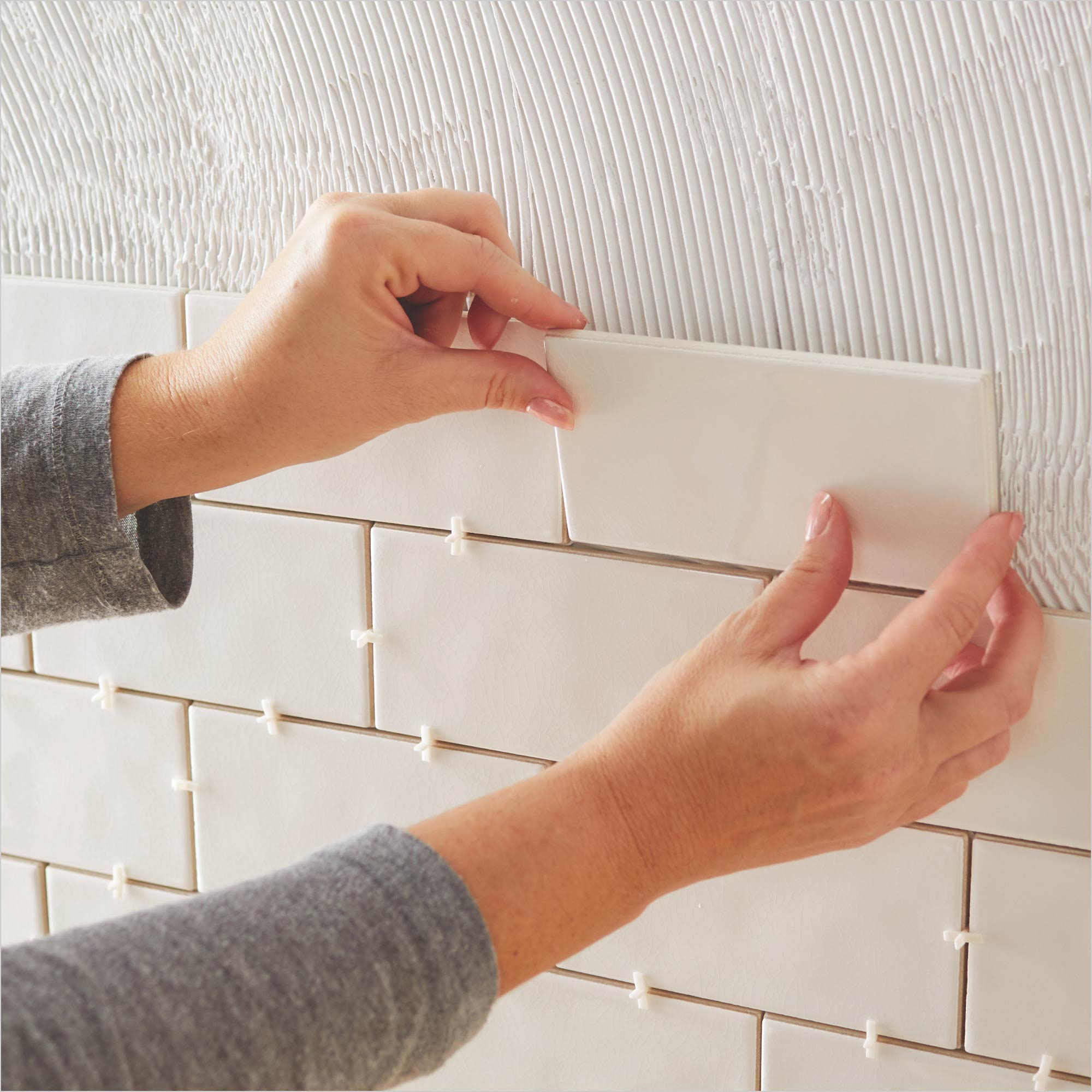 A person applies tile to a wall.