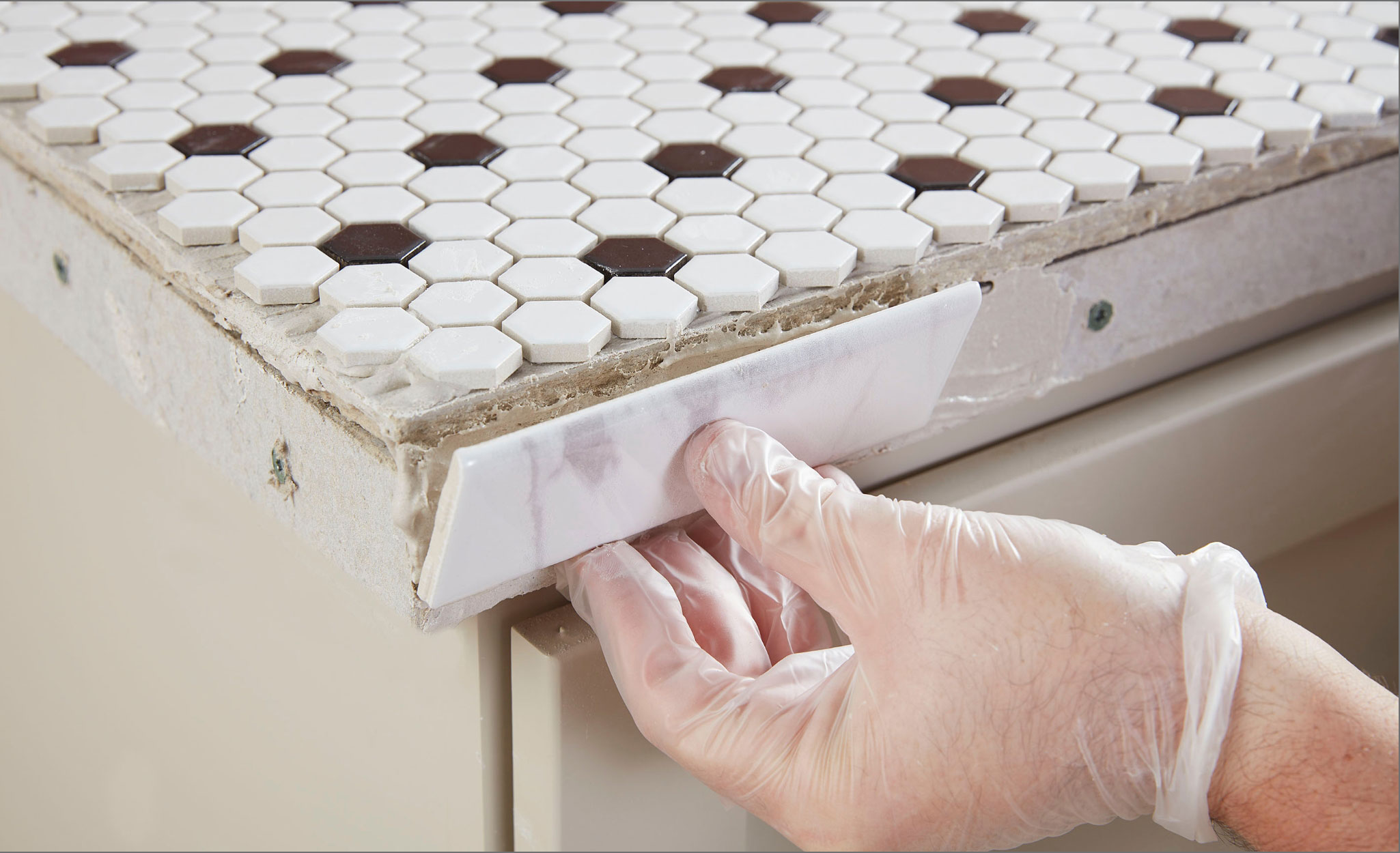 A person applies bullnose tile to the side of a counter.