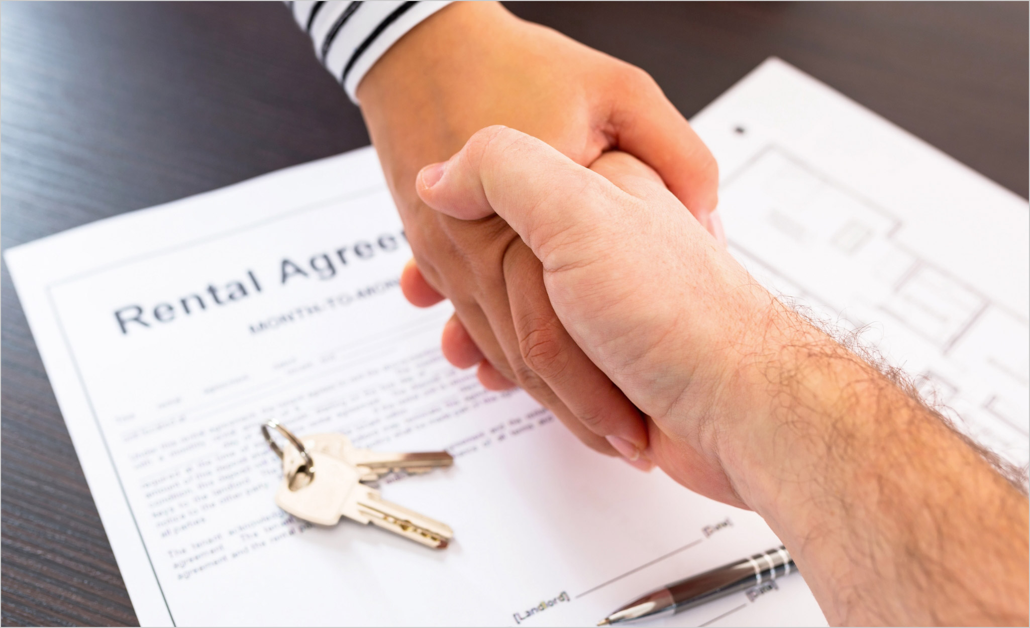 Two people shake hands over a rental agreement.