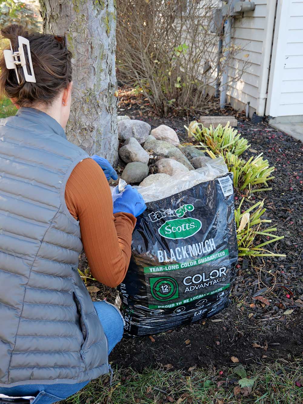 A woman opening a bag of mulch for her garden bed.