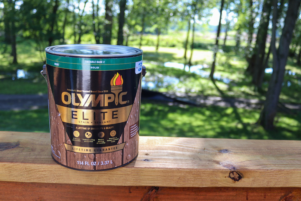 A can of Olympic Elite Solid Stain sitting on a deck rail.