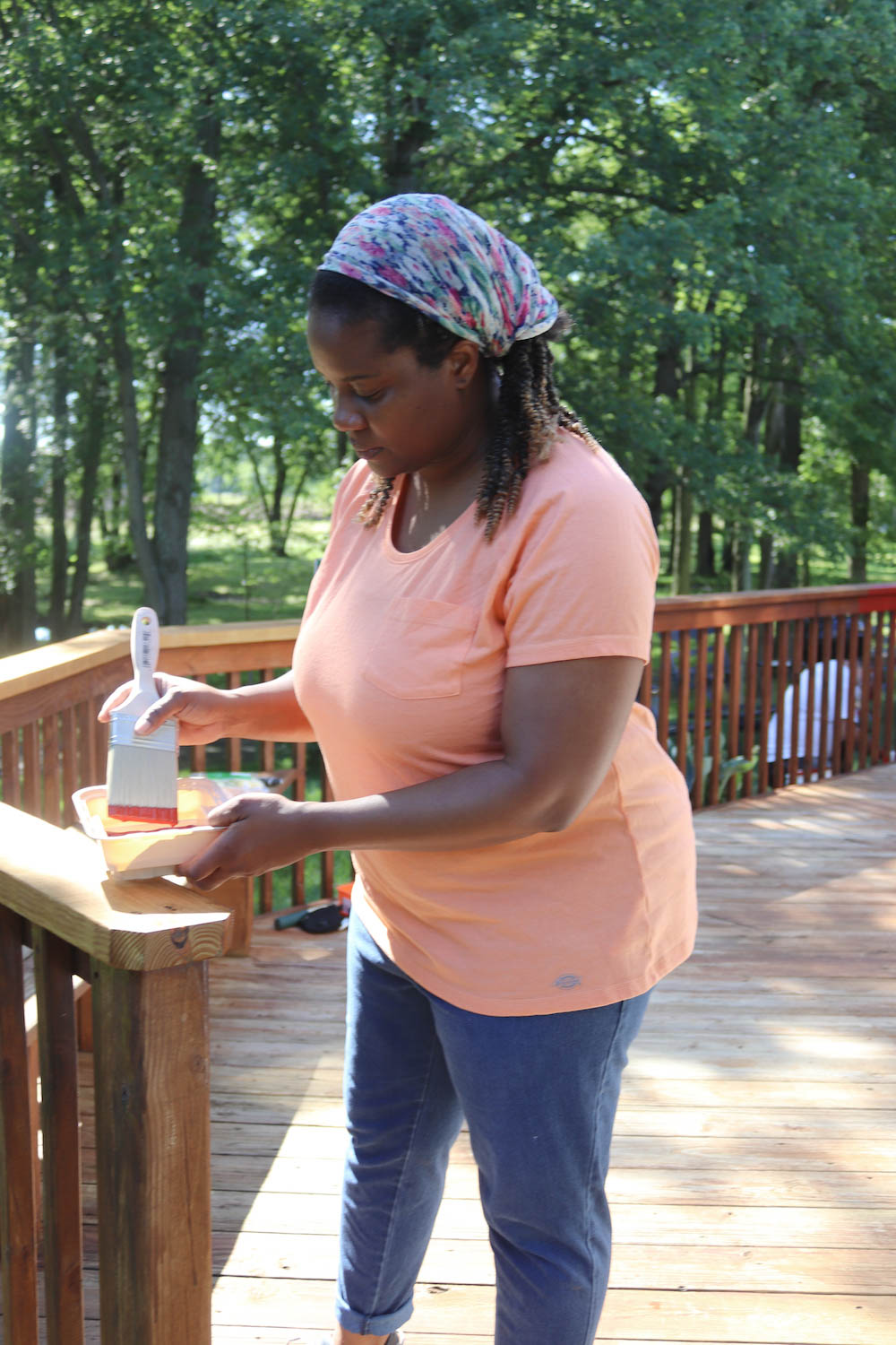 A woman dips a paint brush into a paint tray.