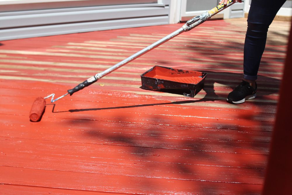 A deck floor is stained red with a large roller.