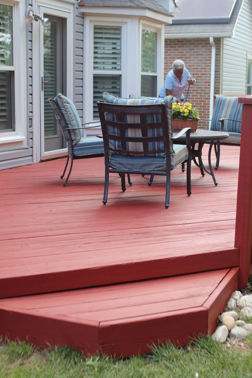 A woman standing on a red stained deck with patio furniture.