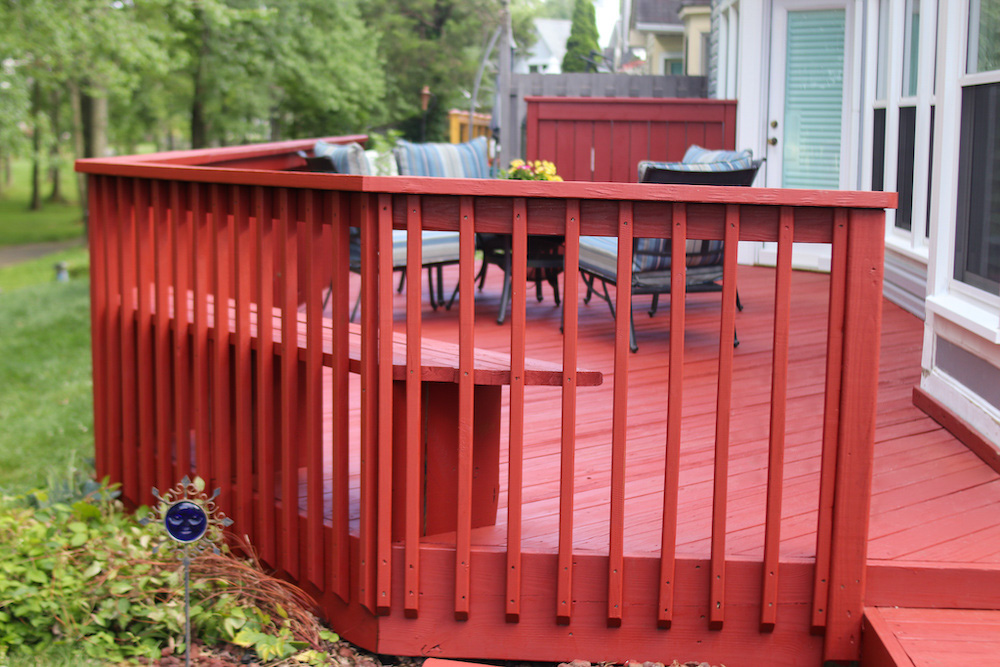 A back deck stained in red is decorated with patio furniture.