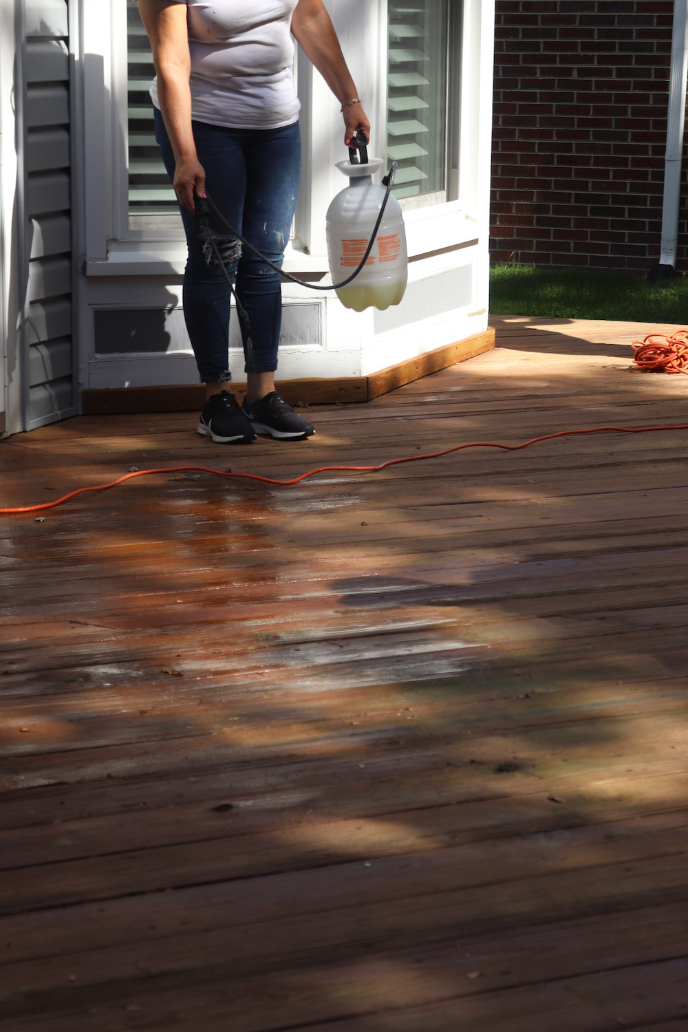 A person using a pump sprayer to spray a deck floor.