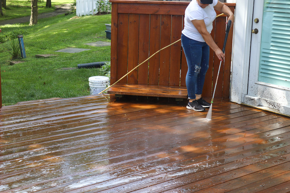 A woman uses a water hose to spray down a deck floor.