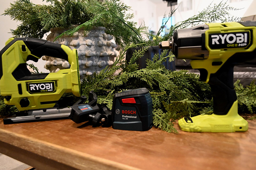 A set of cordless Ryobi tools sitting on a countertop next to pine tree branches.