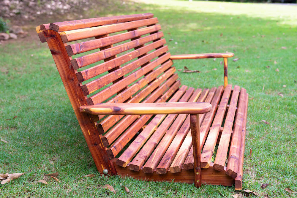 A weatherproofed exterior wooden swing sitting on grass.
