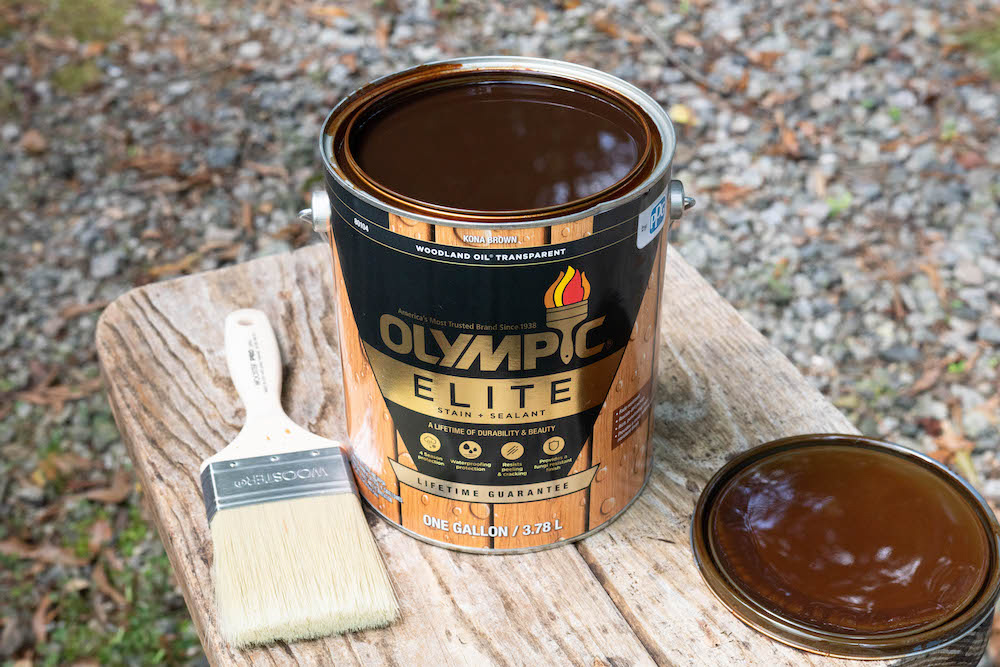 A paintbrush and a can of Olympic Elite Stain and Sealant.