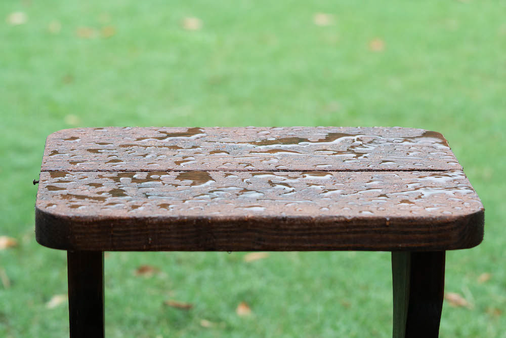 A weatherproofed wooden table with water sitting on top.