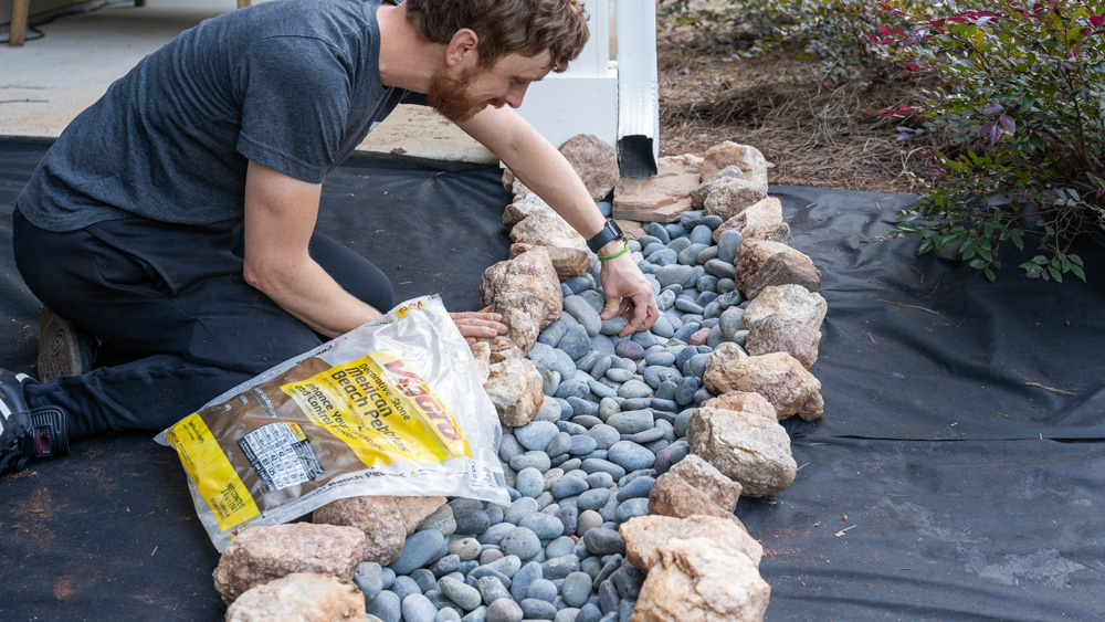 Close up of a man spreading gravel with larger rocks surrounding.