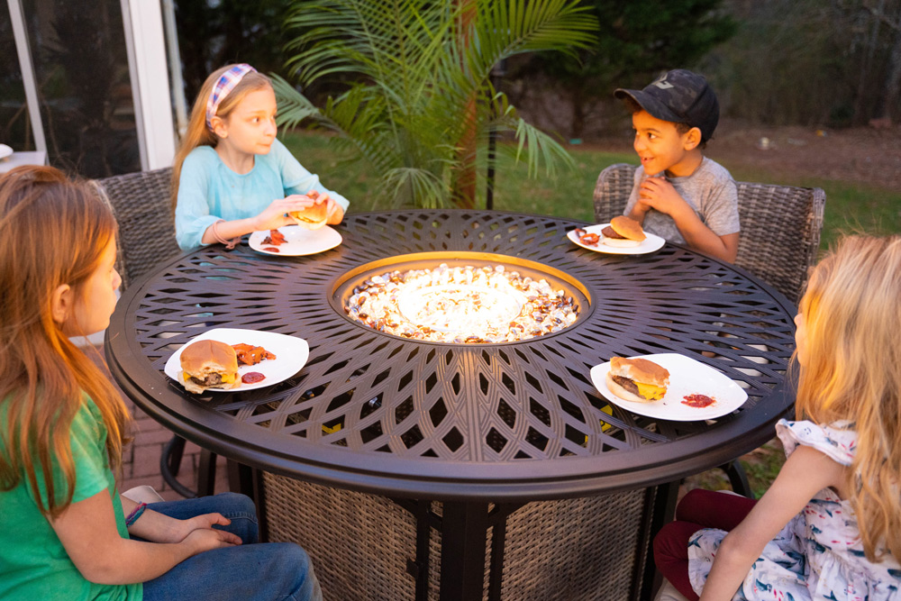 Four children sitting around the firepit table eating their burgers. Four children sitting around the firepit table eating their burgers.