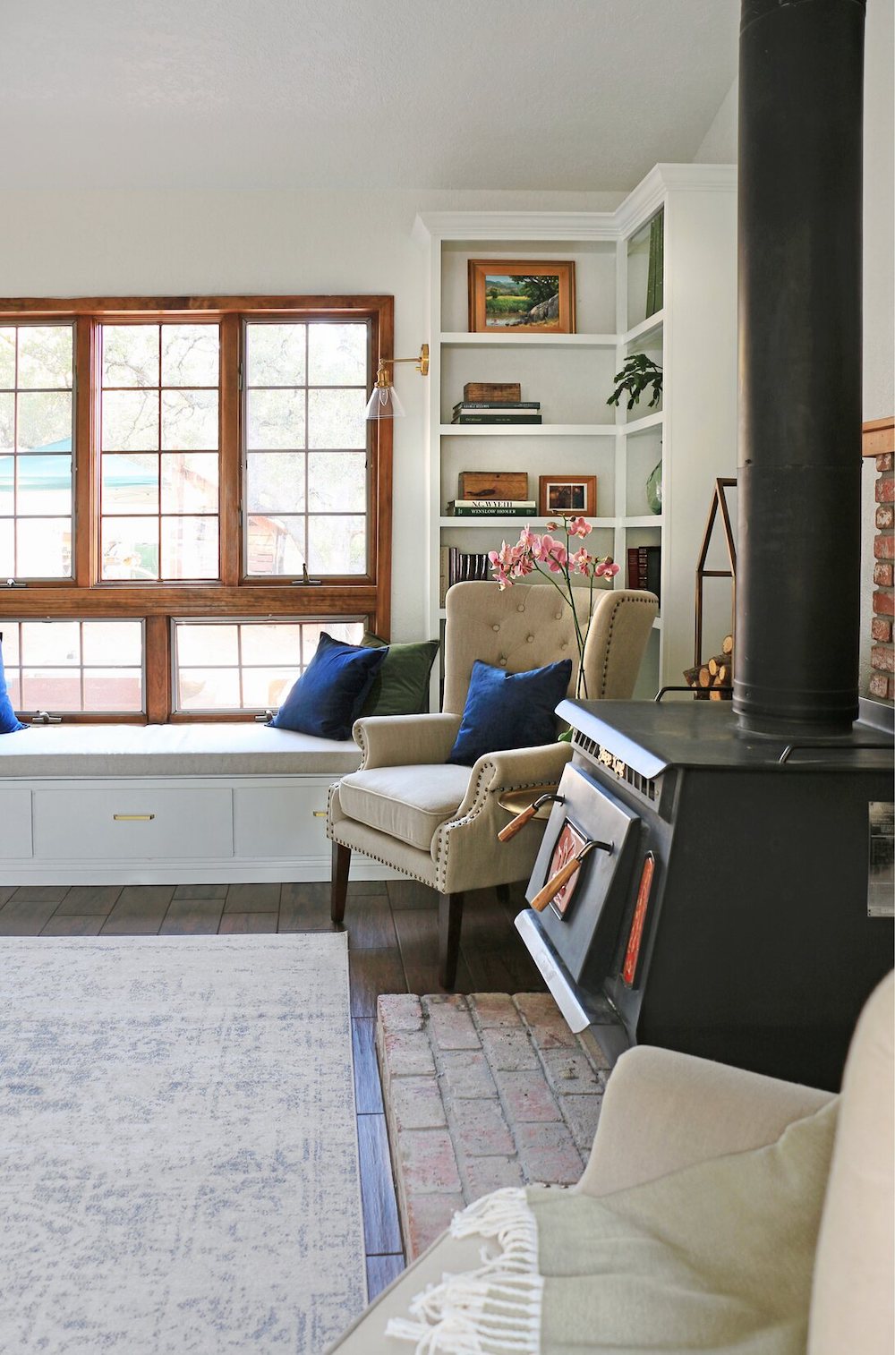 Beige chair placed in the corner with an open window on the left and black antique fireplace on the right