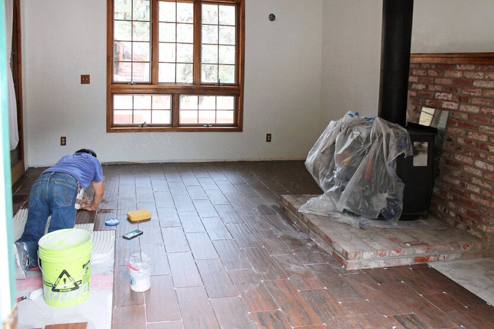 Man installing hardwood flooring to the left with an antique black fireplace on the right side of the shot