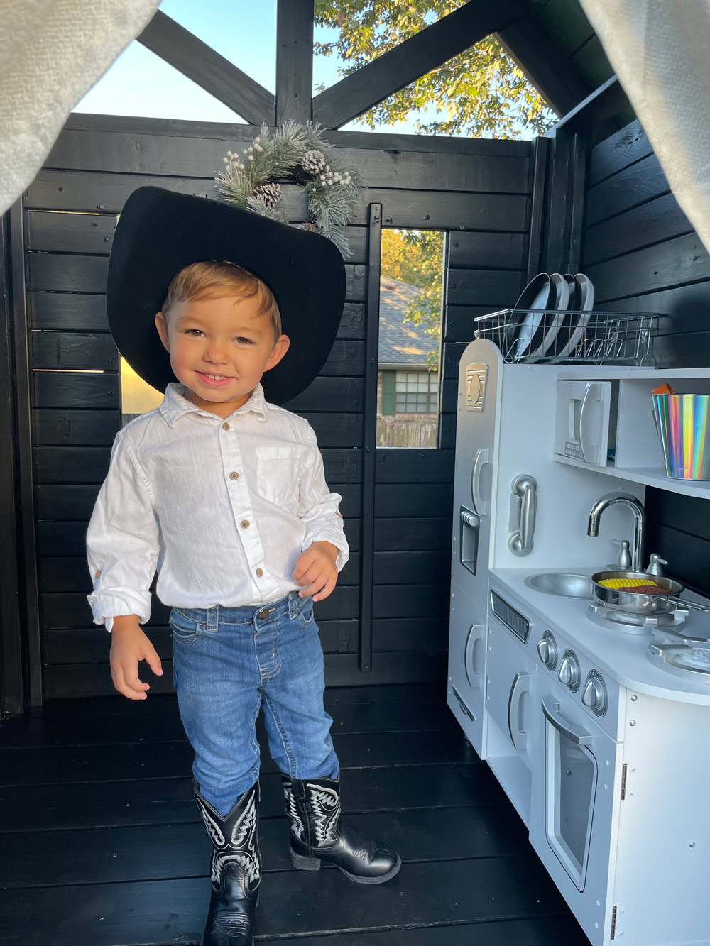 A child standing in a playhouse room with a play kitchen. A child standing in a playhouse room with a play kitchen.