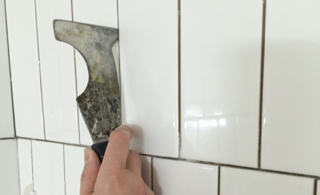 A person removes dirty grout between tiles.