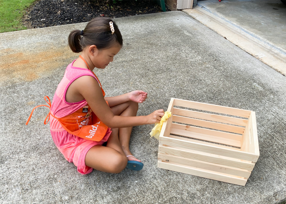 Child wiping wooden crate with a cloth.