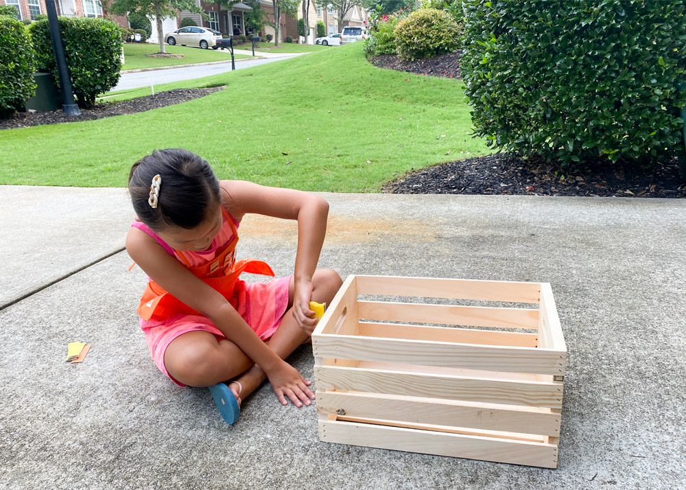 Child on ground sanding wooden crate.