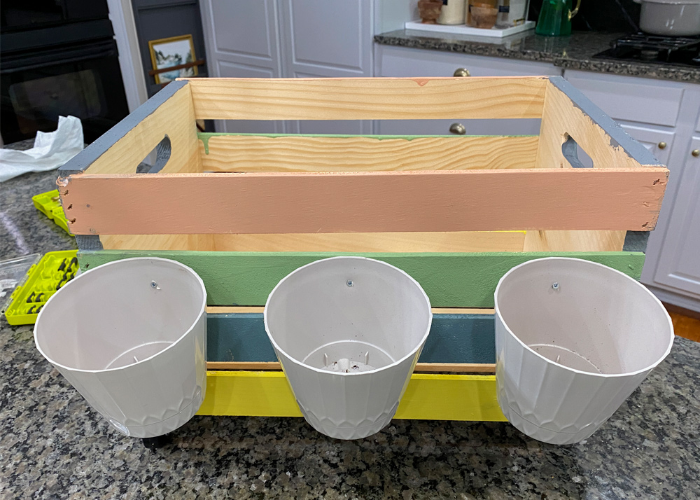 Measure about 1 inch from the top of the planter and use your drill bit to create a small hole in the plastic planter. Figure out exactly where you want the planters to be placed on the wooden crate. 
