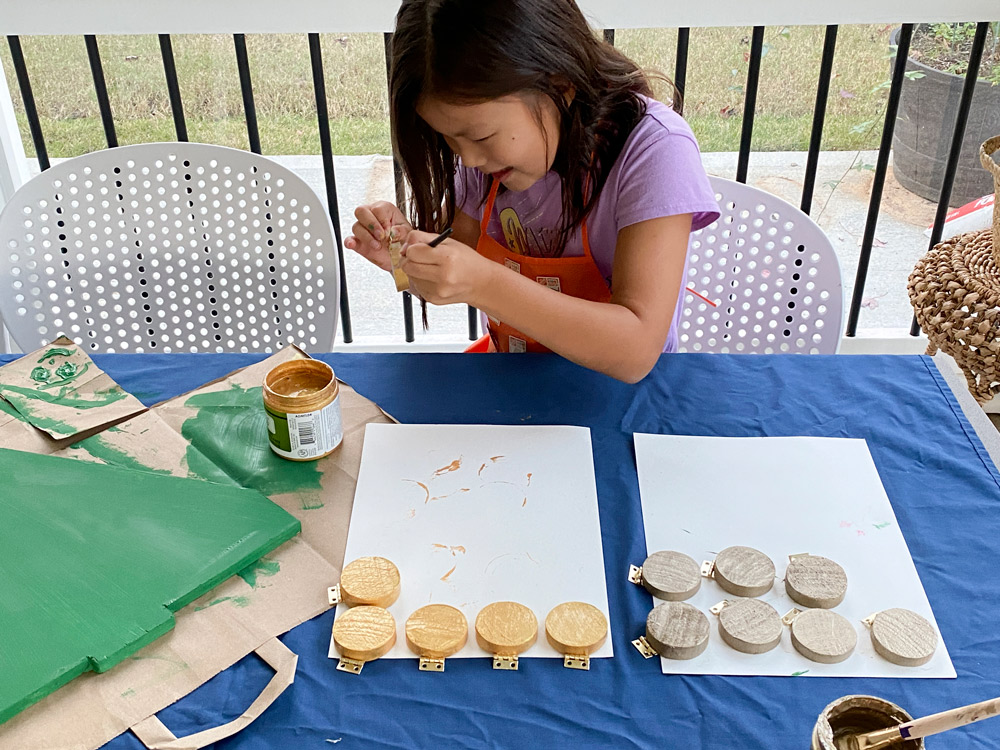 A girl using gold paint to paint round wooden pieces.