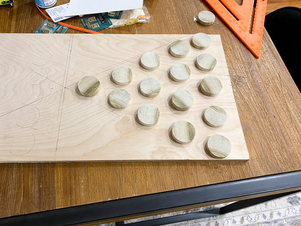Round wooden pieces laid out on a plywood board with pencil tracings.