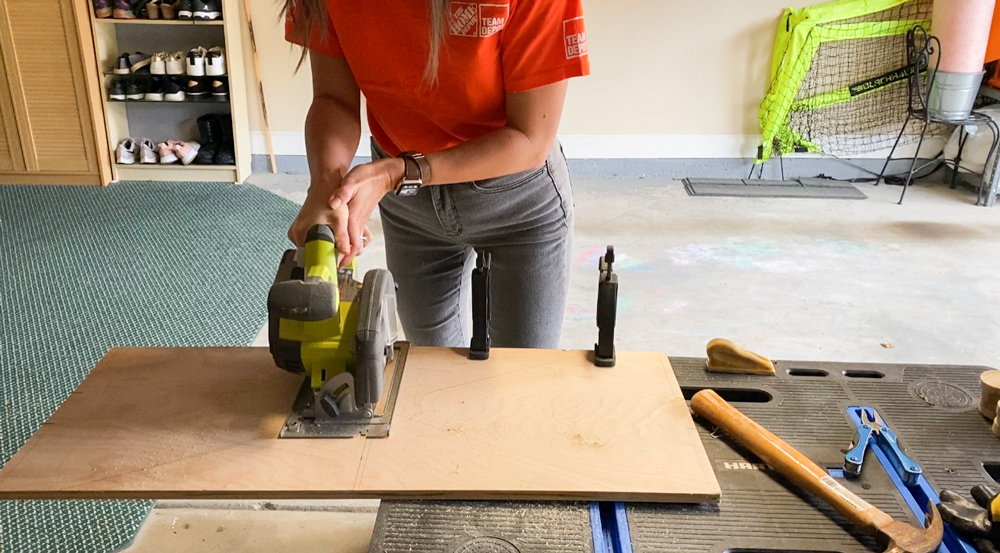 A woman using a circular saw to cut a plywood board.