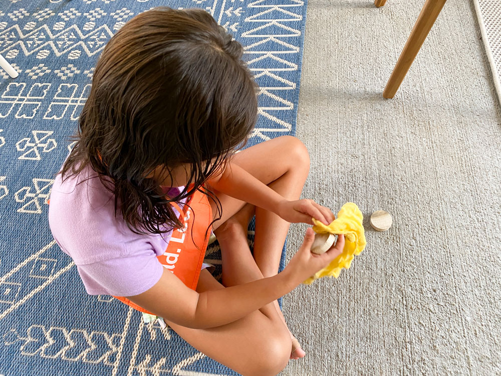 A girl cleaning a round wooden piece with a tack cloth.