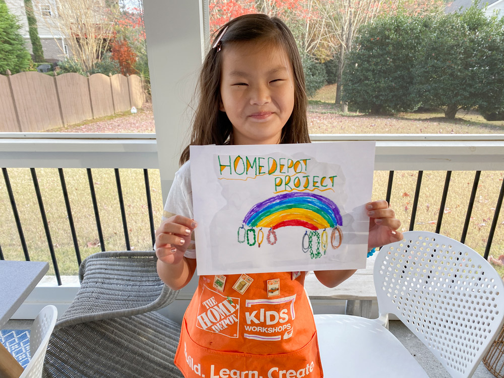 A girl holding a drawing of a DIY Rainbow Jewelry Holder project.