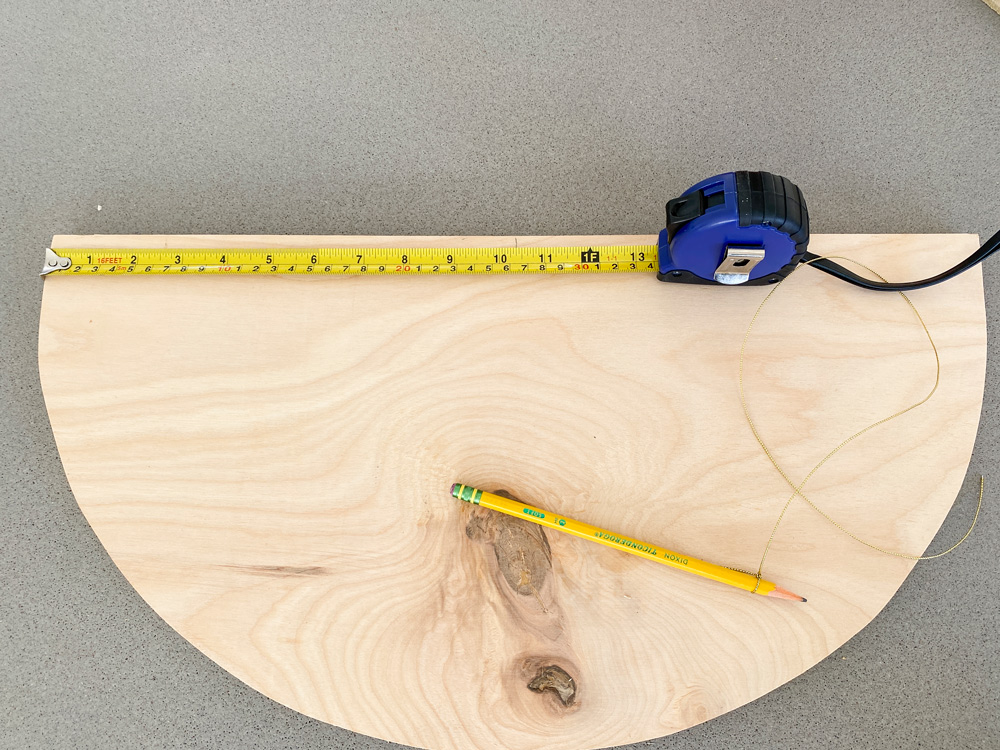 A measuring tape and a pencil lying on a half-moon–shaped piece of plywood.