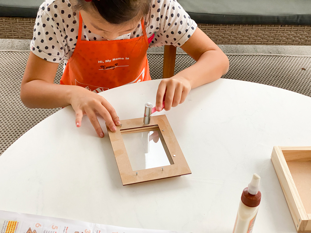 A girl nailing a frame for a DIY Valentine’s Day Box with a small mallet.