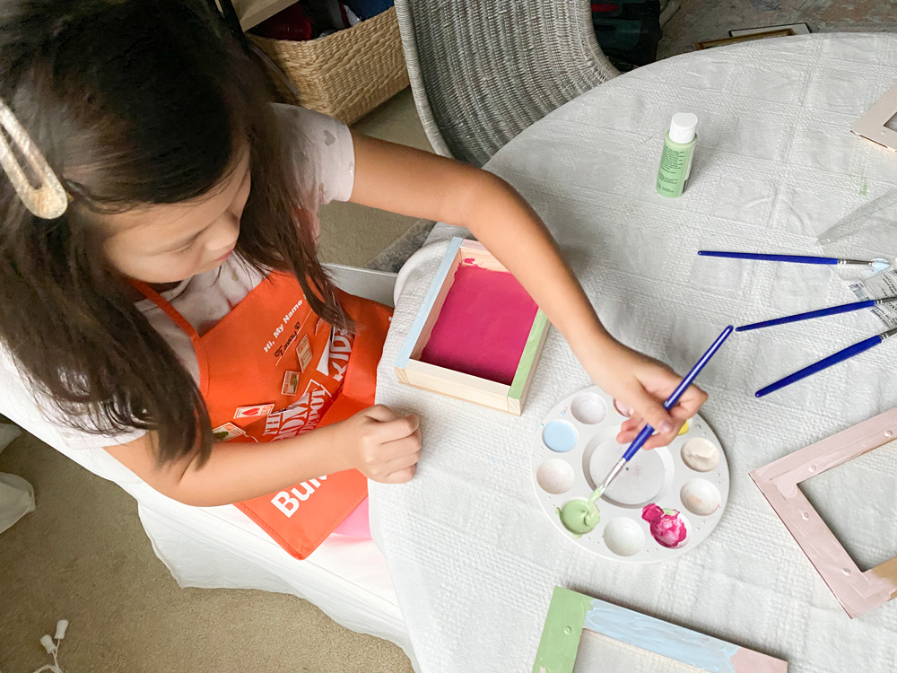 A girl using pastel paints to paint the inside of a DIY Valentine’s Day Box.