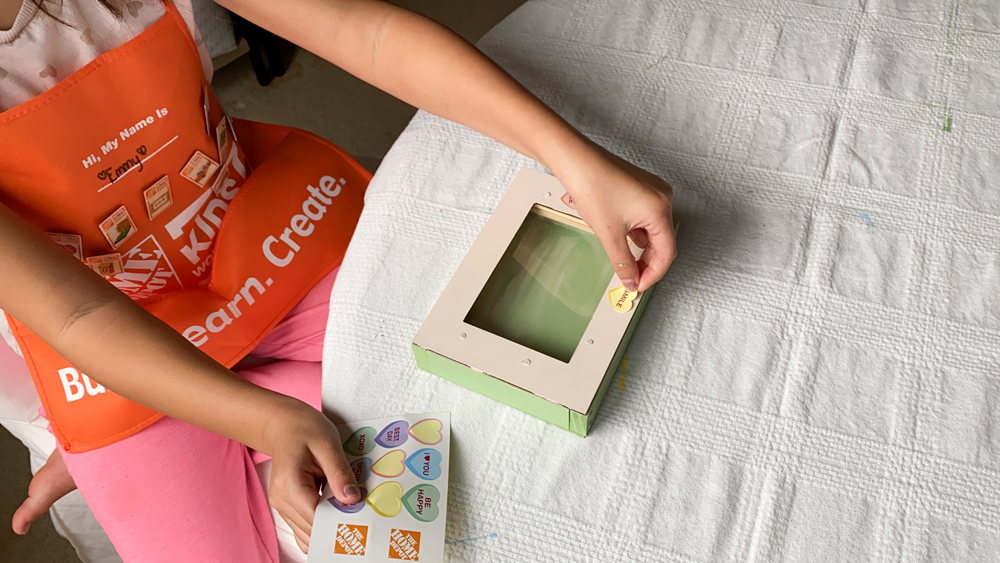 A girl attaching heart-shaped stickers to a DIY Valentine’s Day Box.
