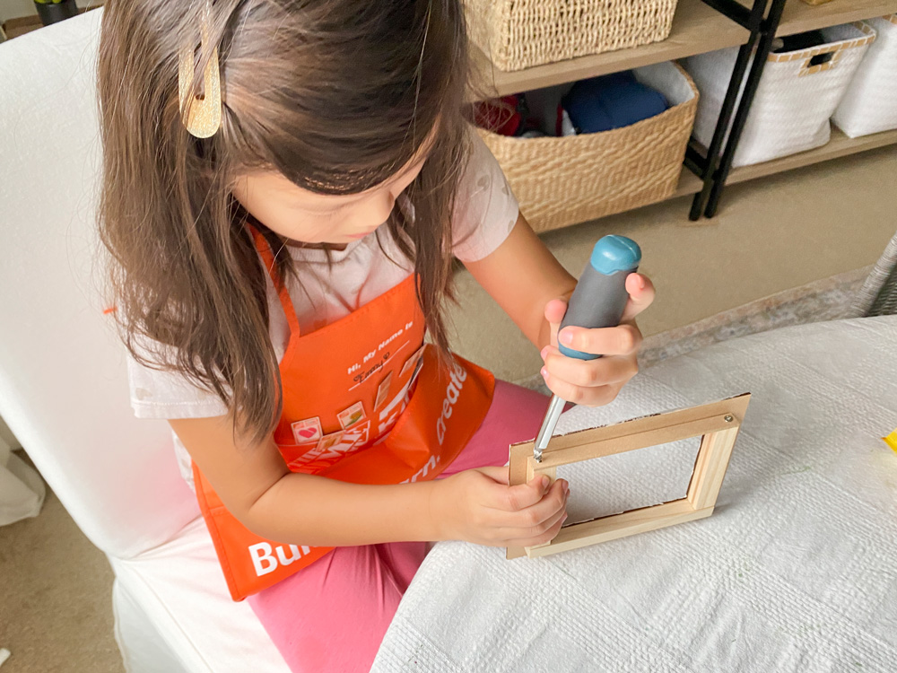 A girl using a screwdriver to screw a photo frame for a DIY Valentine’s Day Box.