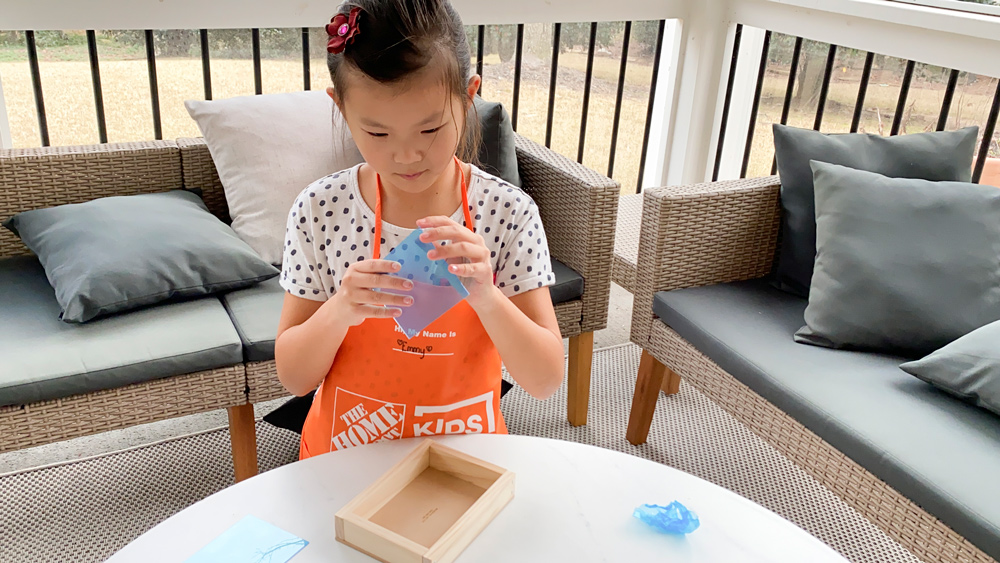 A girl peeling a blue protective layer off of a small, clear plastic sheet.