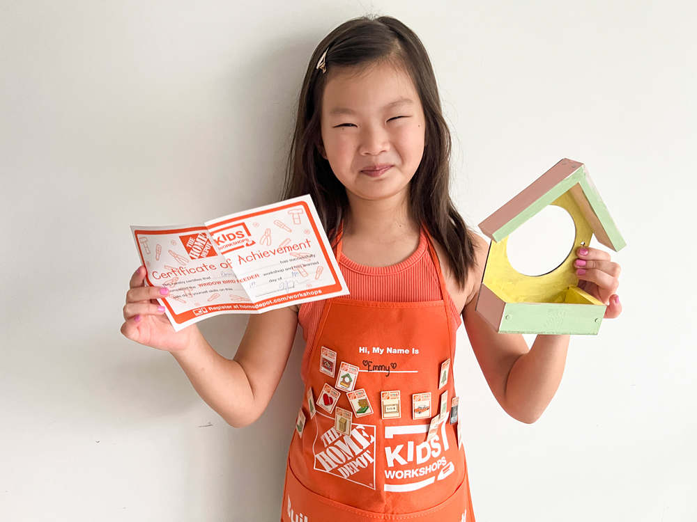 A girl holding a certificate of achievement and a completed window bird feeder.