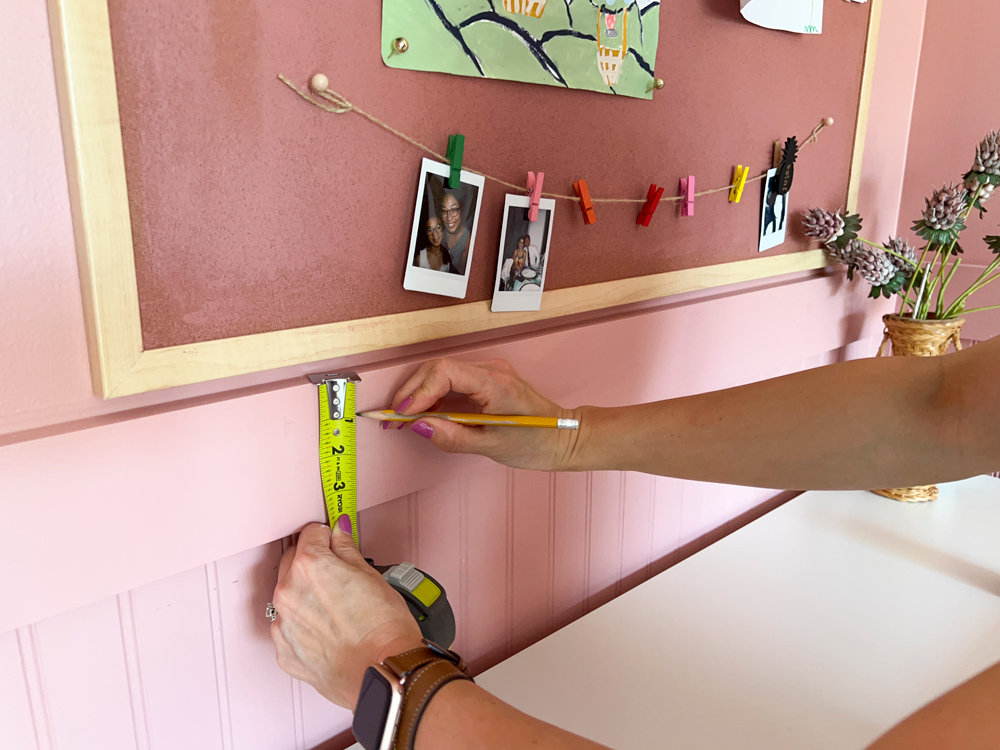 A person using a pencil and tape measure to mark the towel bar placement.