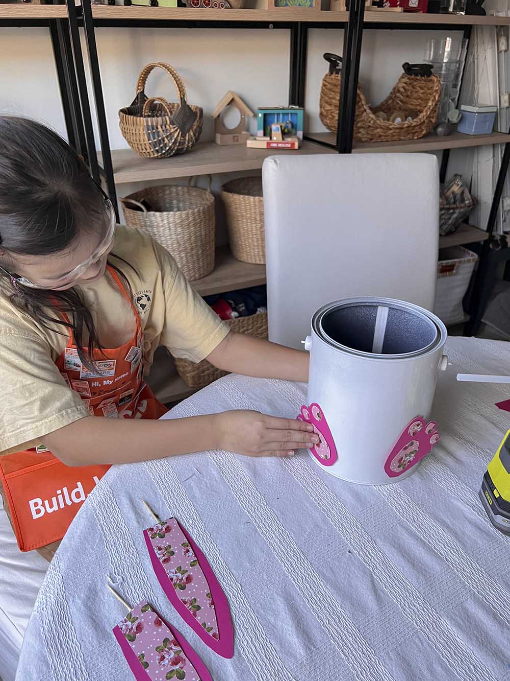 Girl placing paper cut outs of bunny feet on paint bucket.