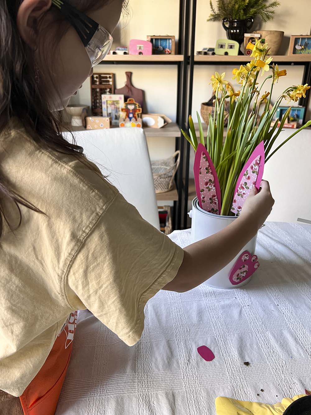 Girl placing paper bunny ears in paint bucket with flowers.