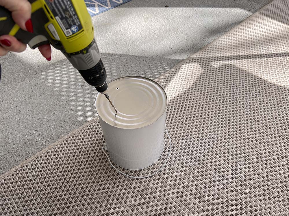 Hand using drill to make holes in the bottom of paint bucket.