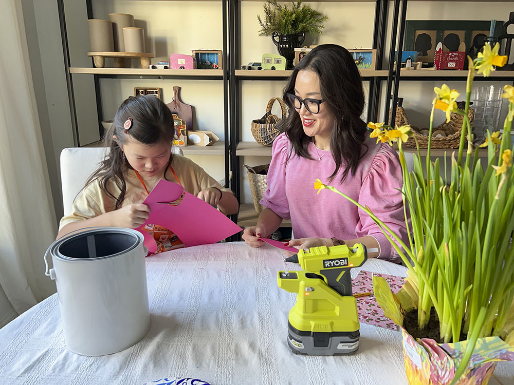Mother and daughter sitting at table while daughter cuts pink paper.