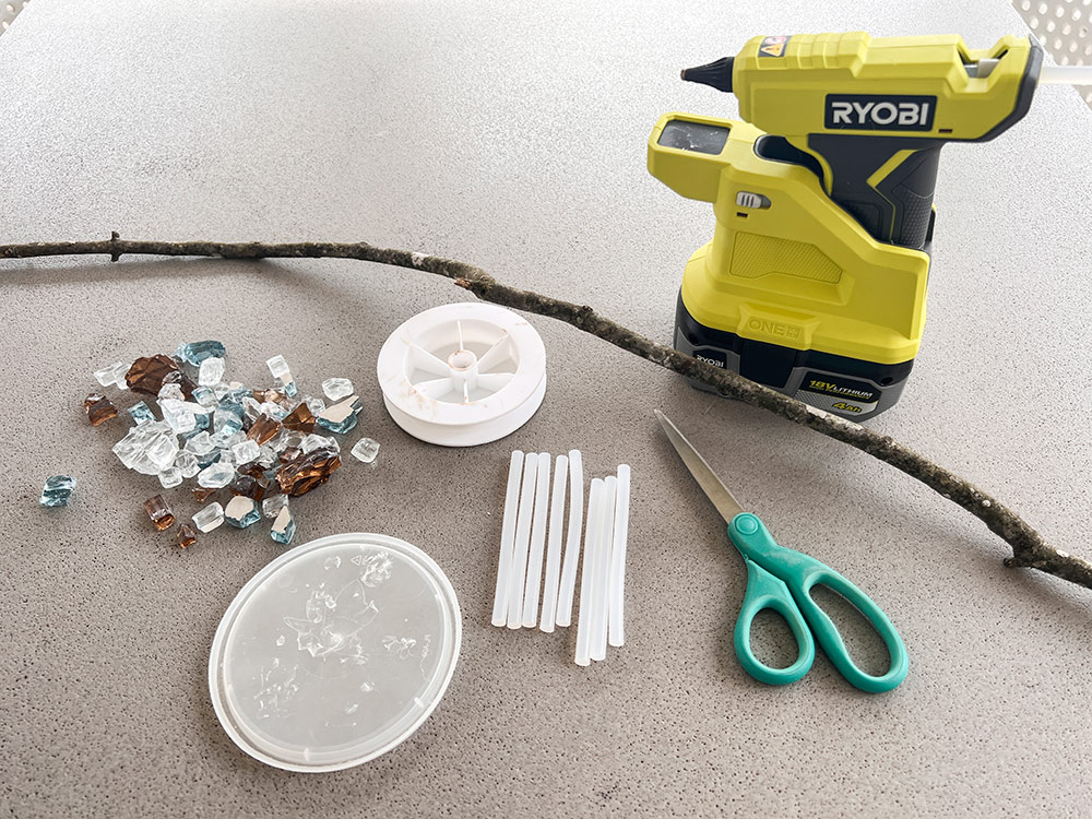 Glue gun, stick, scissors, fire glass, glue and container lid on table.